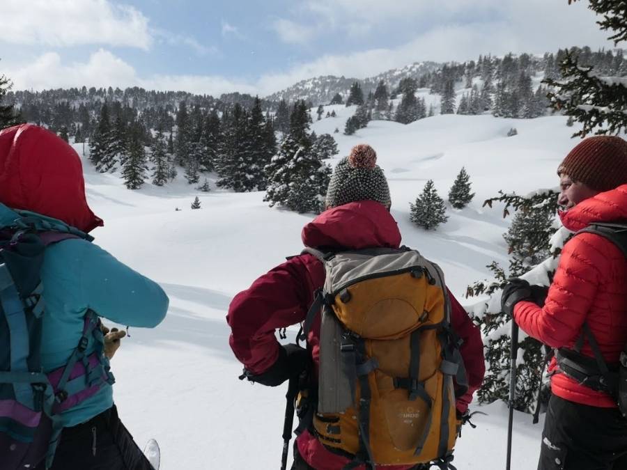 trois personnes discutent devant un paysage enneigé vallonné et boisé