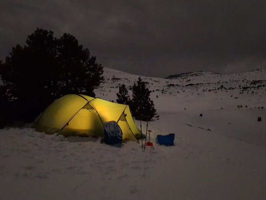 Tente éclairée par la lune et la neige en bivouac hivernal